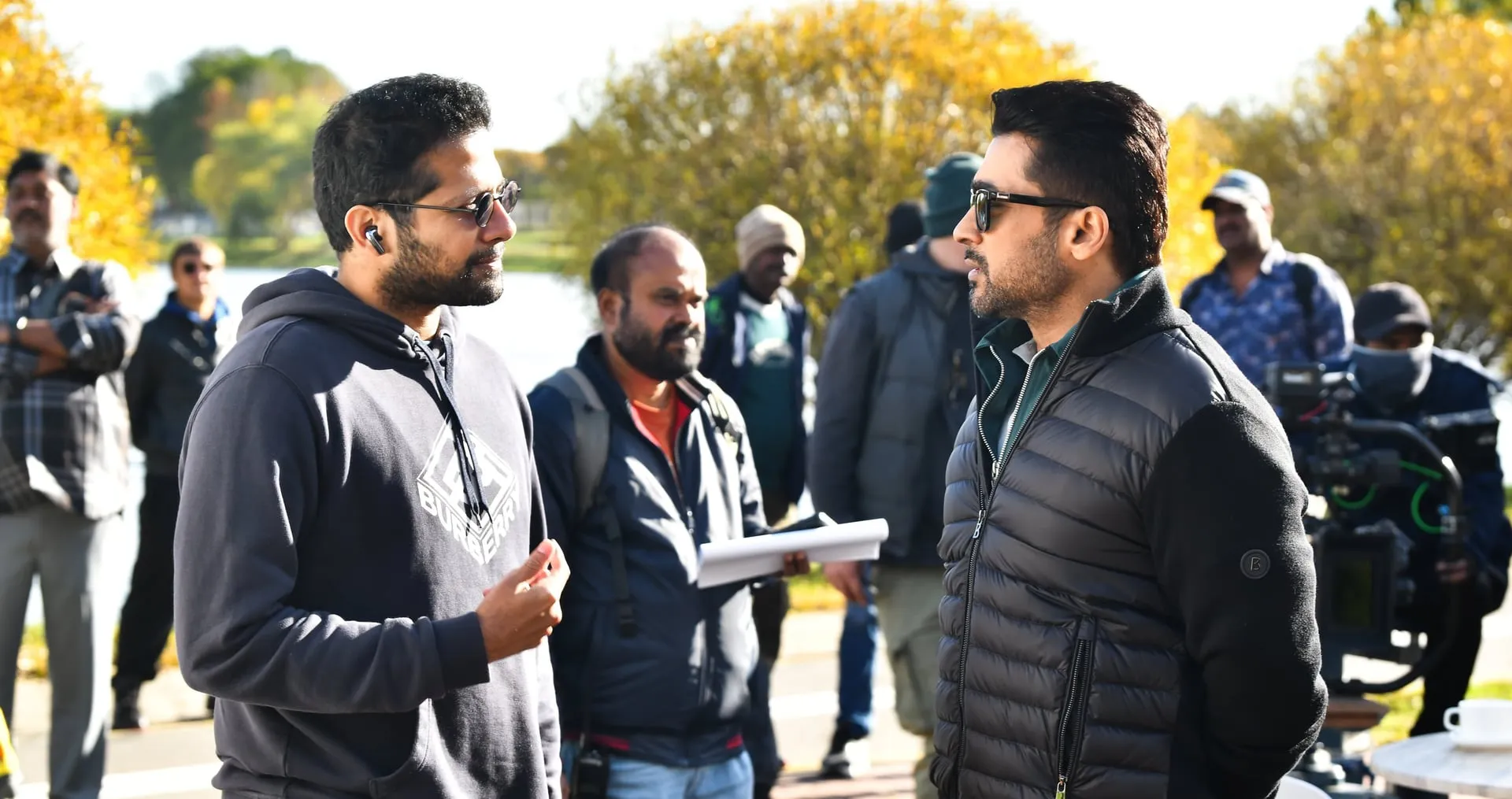 Venky Atluri directs Suriya on an autumn lakeside set of Vishwanath & Sons with the camera crew behind them