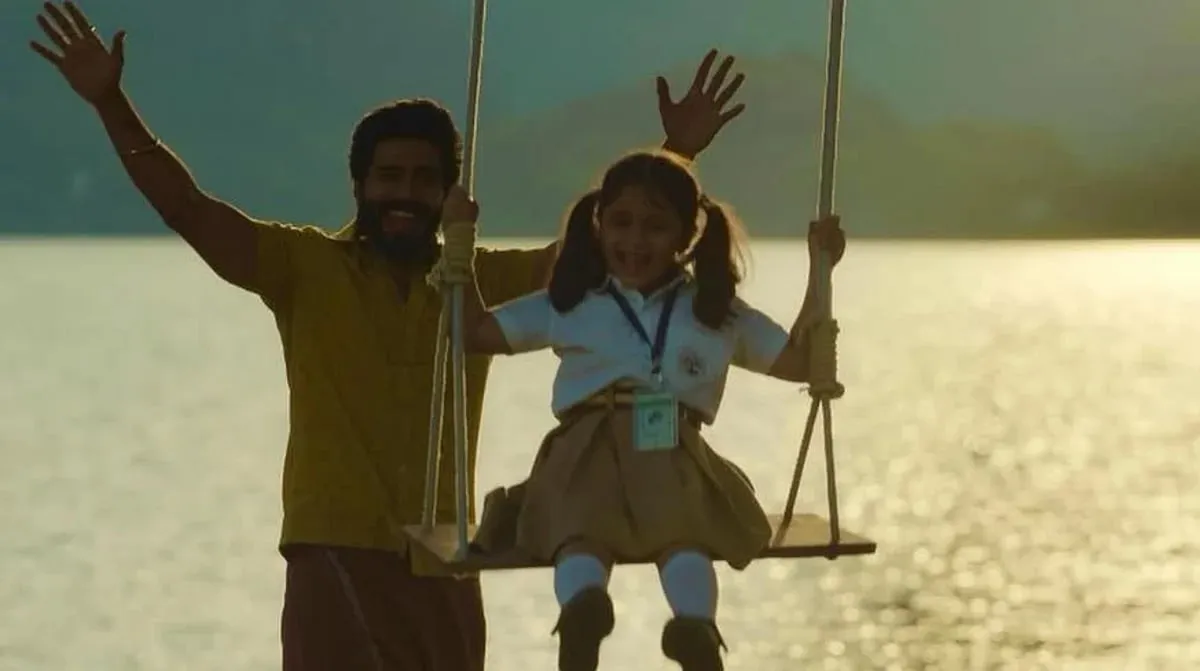 Vishnuu Vishal and the young Mathi laughing on a lakeside swing in a still from Gatta Kusthi 2