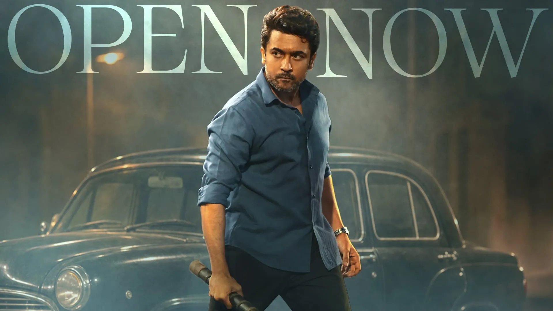 Suriya holds a lathi on a smoky street in front of a vintage Ambassador car on the Vishwanath & Sons bookings poster