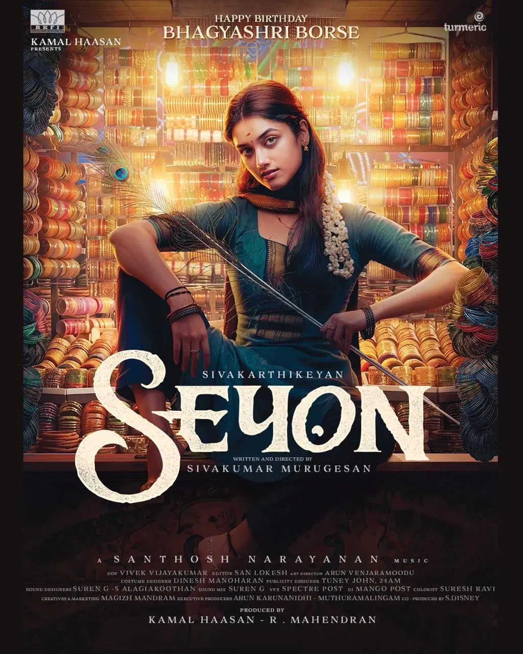 Bhagyashri Borse seated in a bangle shop on the Seyon character poster, peacock feather in hand, with Sivakarthikeyan's name above the title