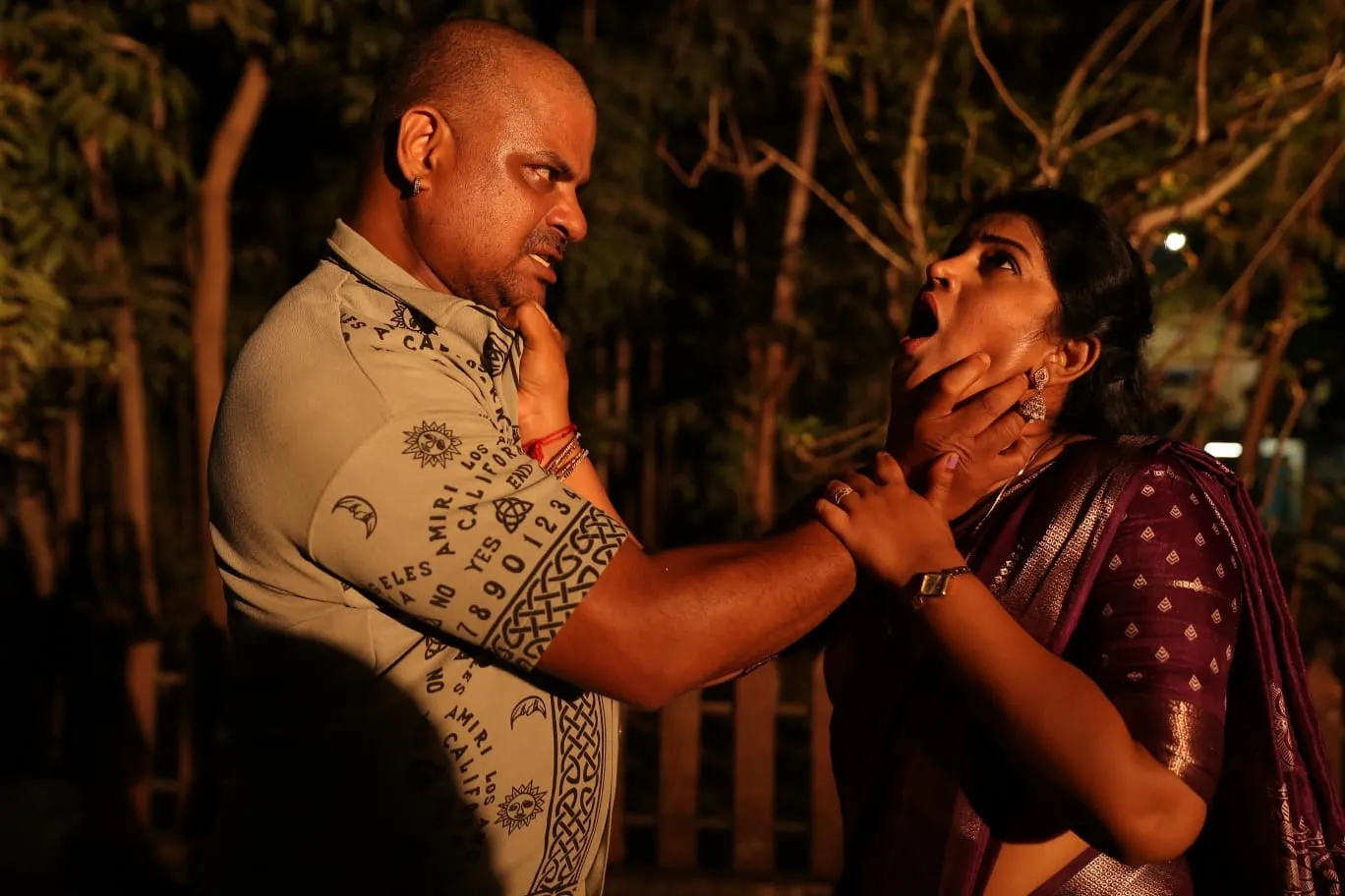 Inba grips a woman by the throat in a dim, tree-lined yard at night in Samharam