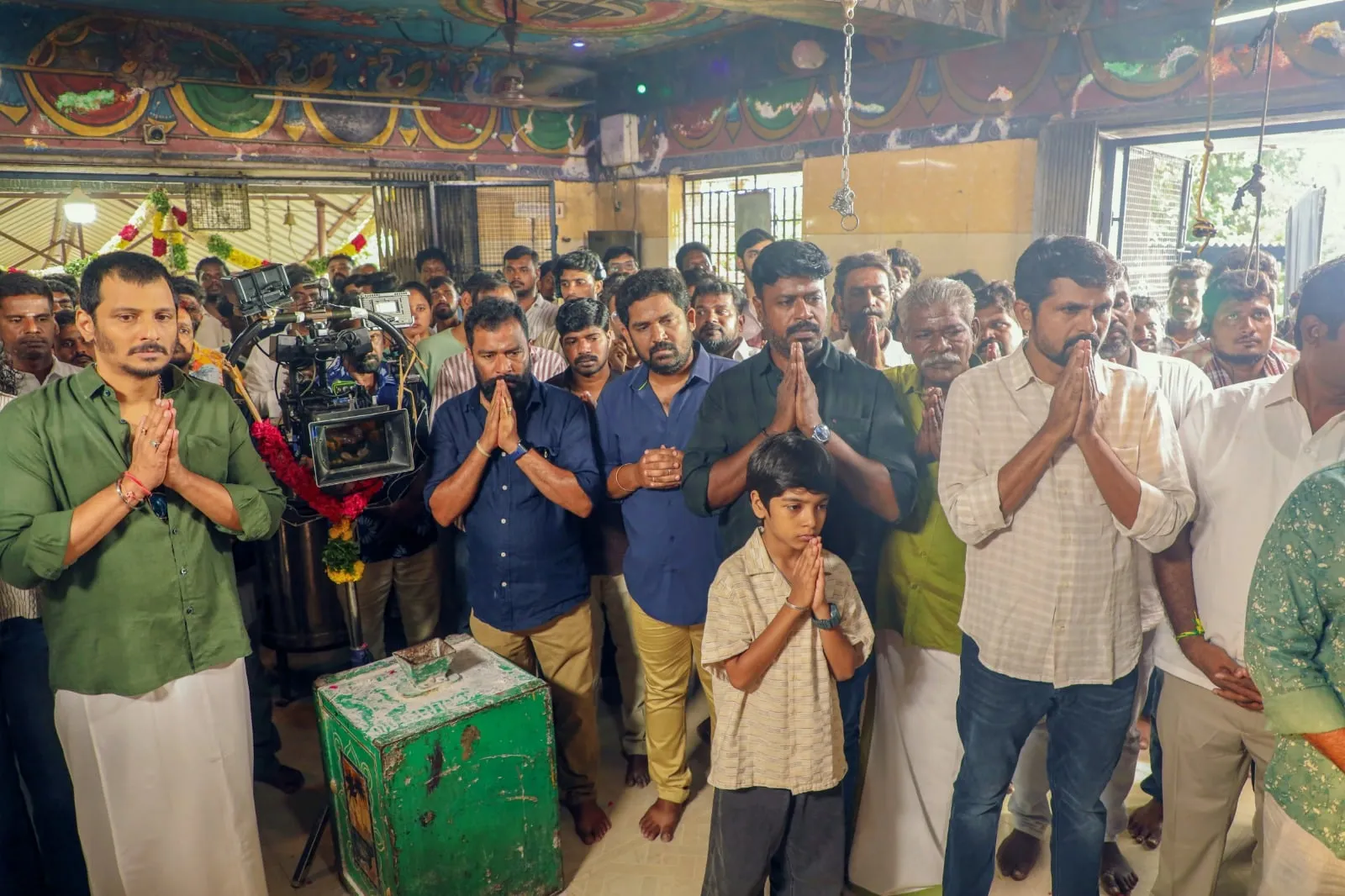 Jiiva and the Thagappan unit with hands folded at the launch pooja, the film's camera garlanded beside them