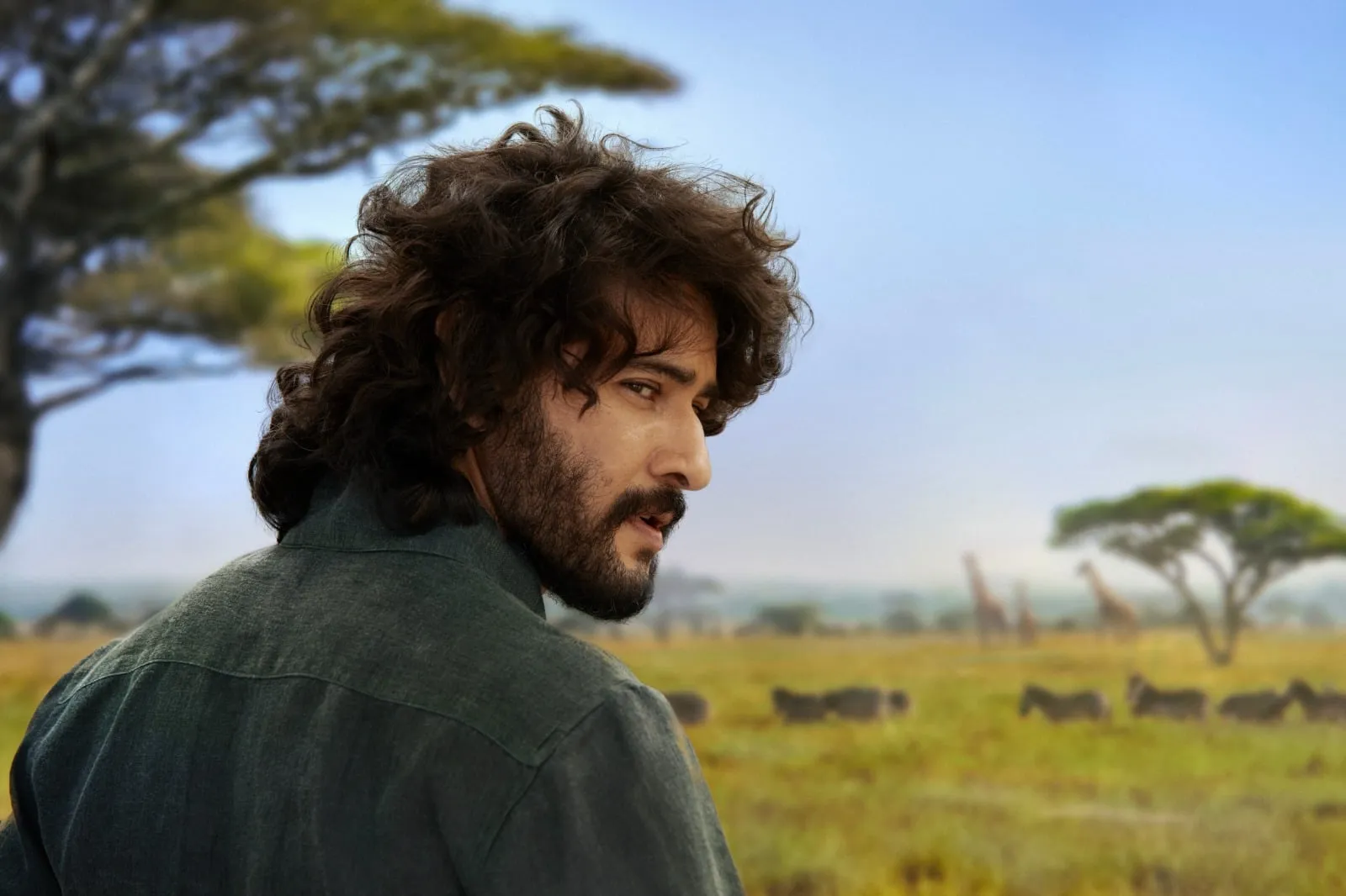 Mahesh Babu as Rudhra looking back across the Maasai Mara plains with giraffes in the distance