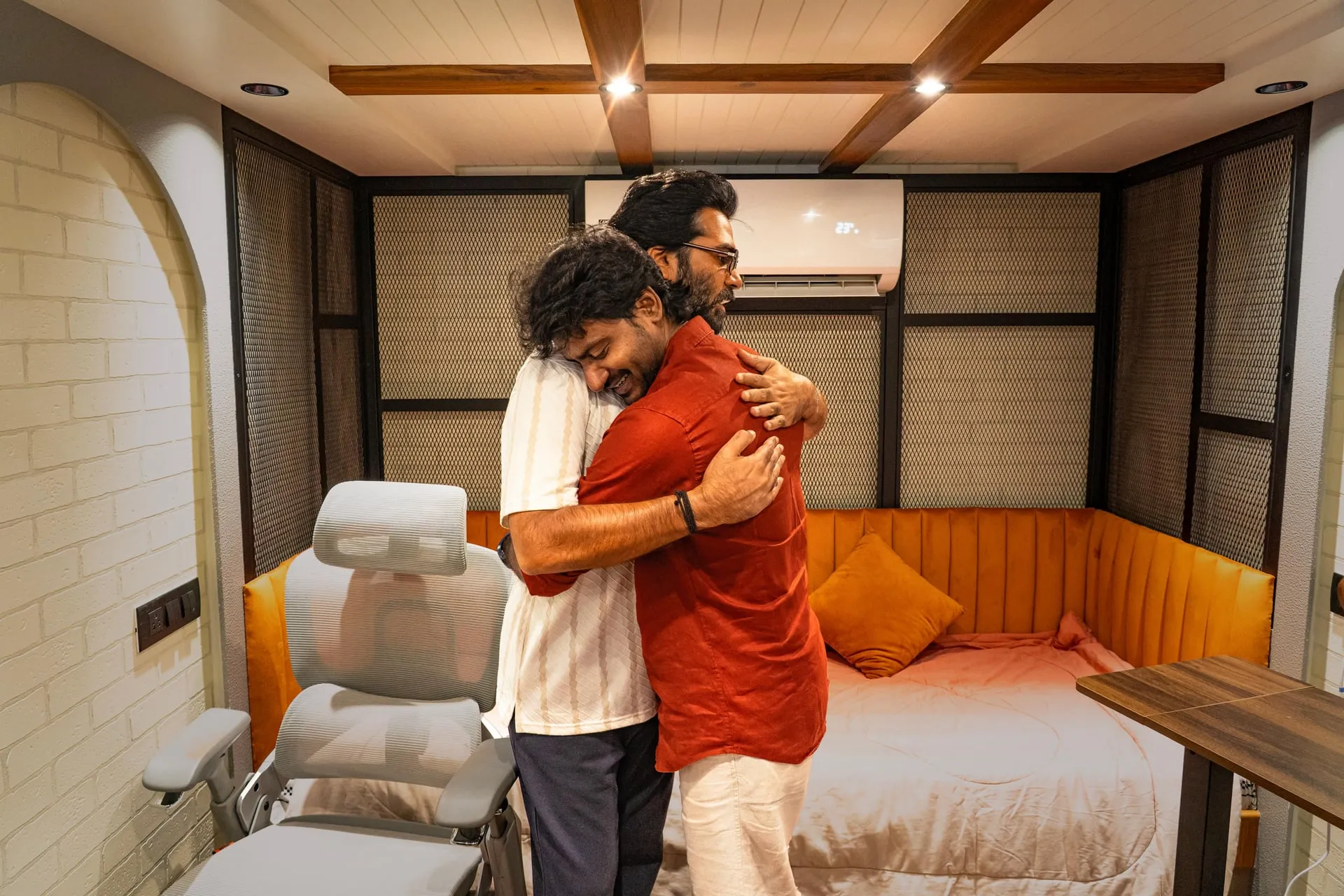 Silambarasan TR and Leo Sivakumar embrace in a room with an orange sofa