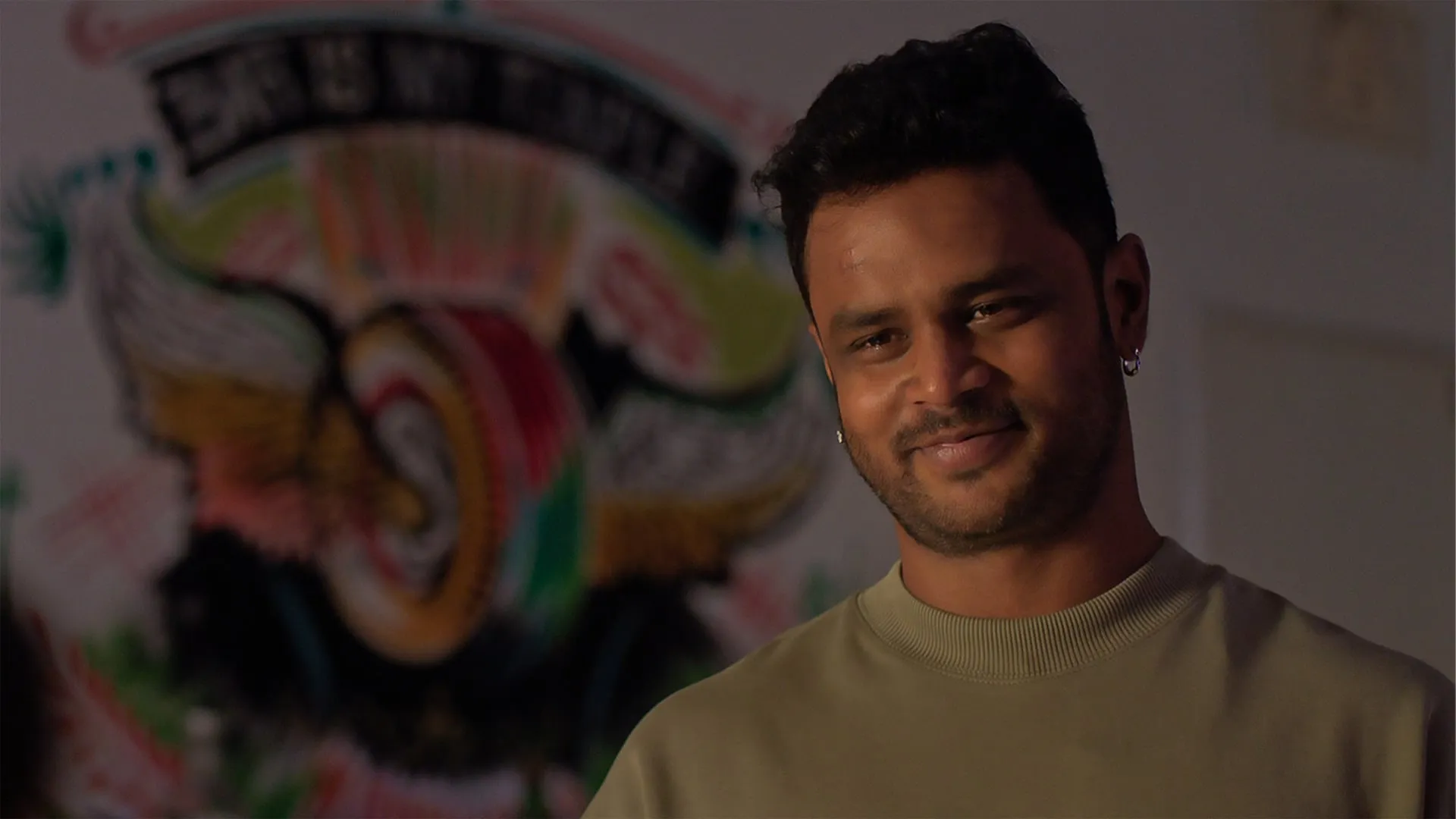 T Anthony smiling in front of a painted mural in a still from Yen Ennai Yetho Seithai