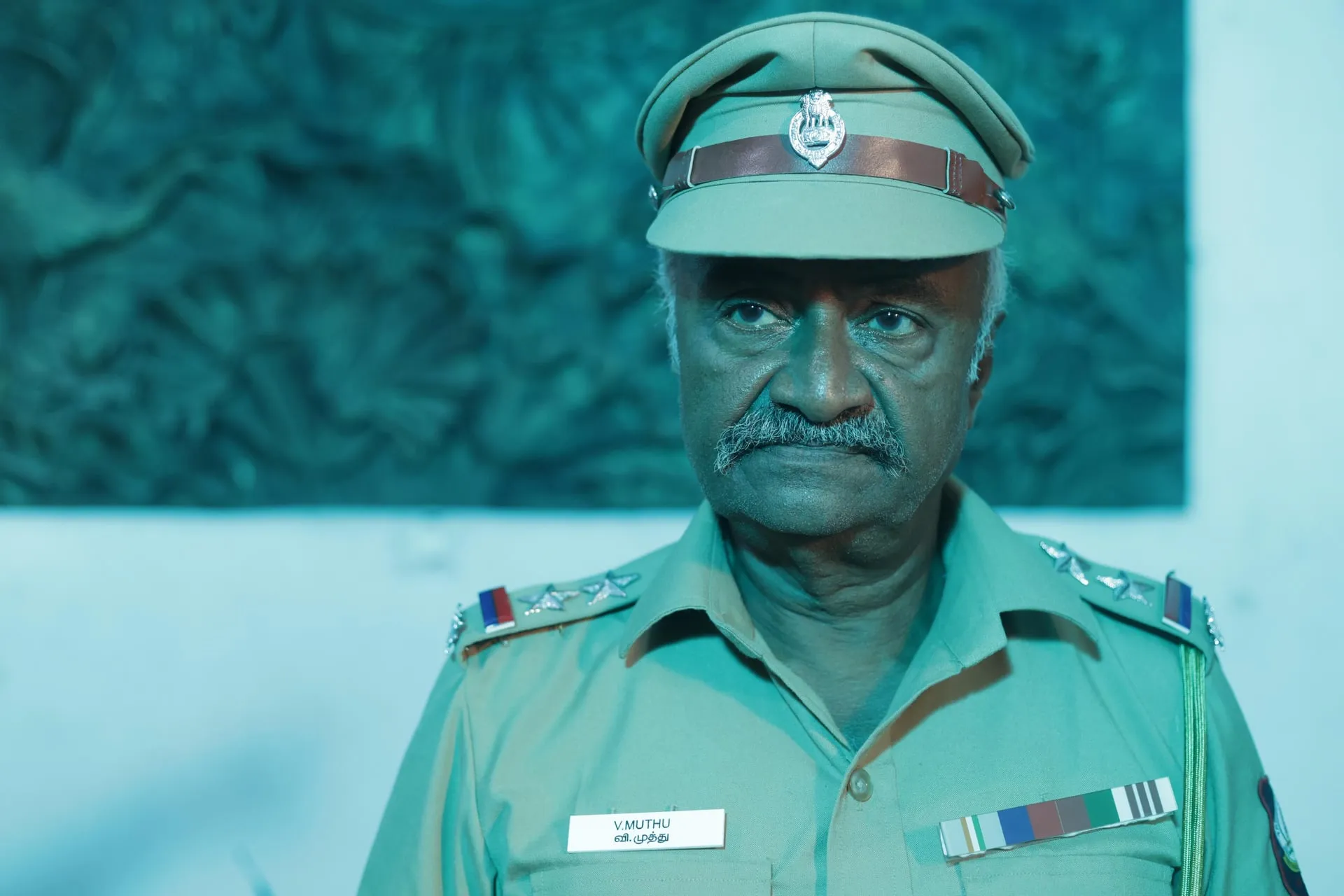 The name tag reads V. Muthu: Bhaskar plays one of two officers who walk into the murder house. M.S. Bhaskar as inspector V. Muthu in Vidiyum Kaathiru