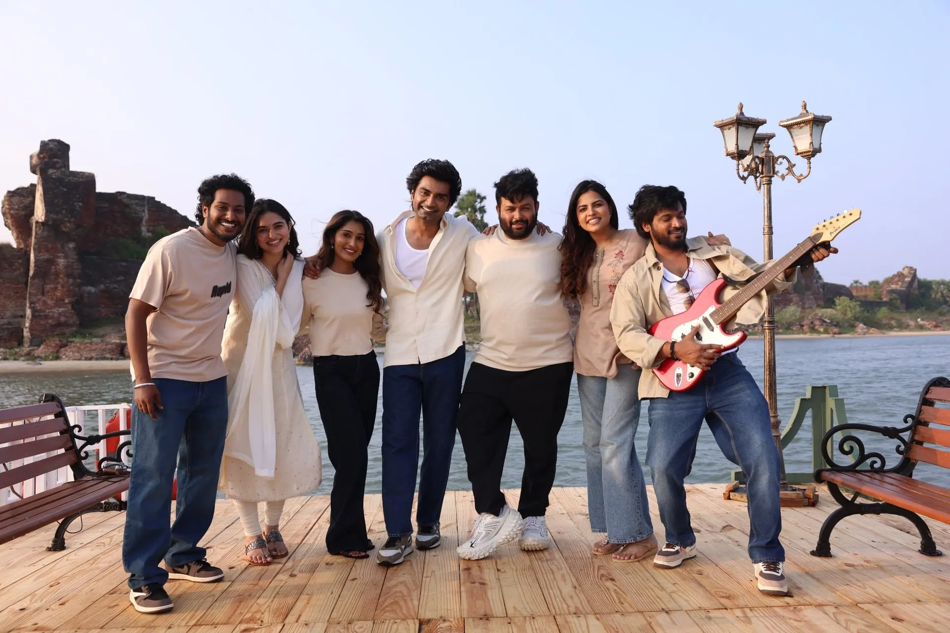 The gang of friends pose together on a wooden jetty by a lake, one of them holding a red electric guitar