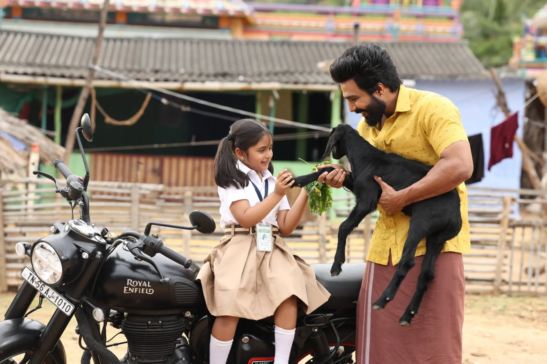 Vishnuu Vishal holds a black goat kid while Zara feeds it greens, seated on a Royal Enfield in Gatta Kusthi 2