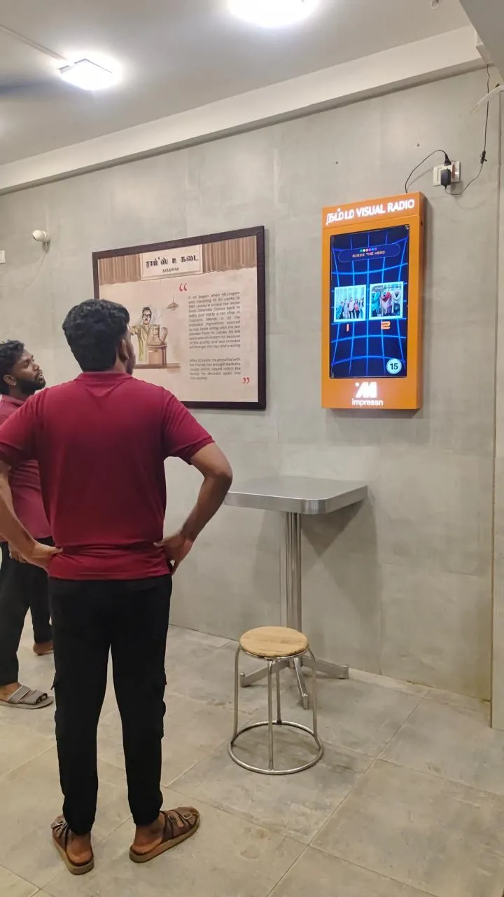 Two men watching an Impressn Visual Radio screen at Ram's Tea Kadai