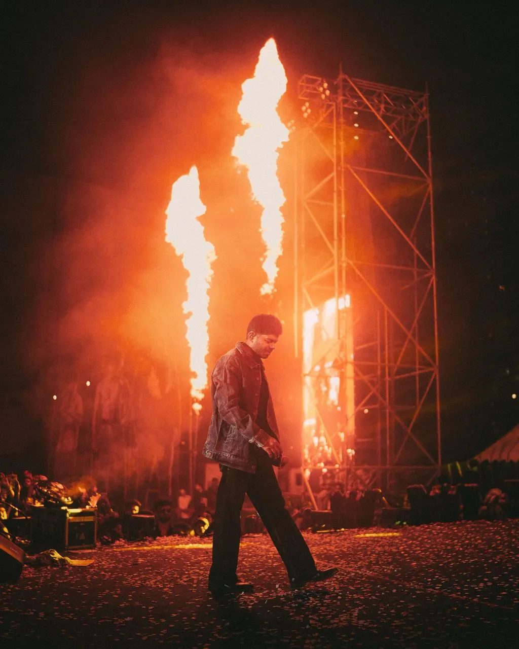 A performer walks the Vanakkam Vanakkam Bengaluru stage with pyrotechnics behind