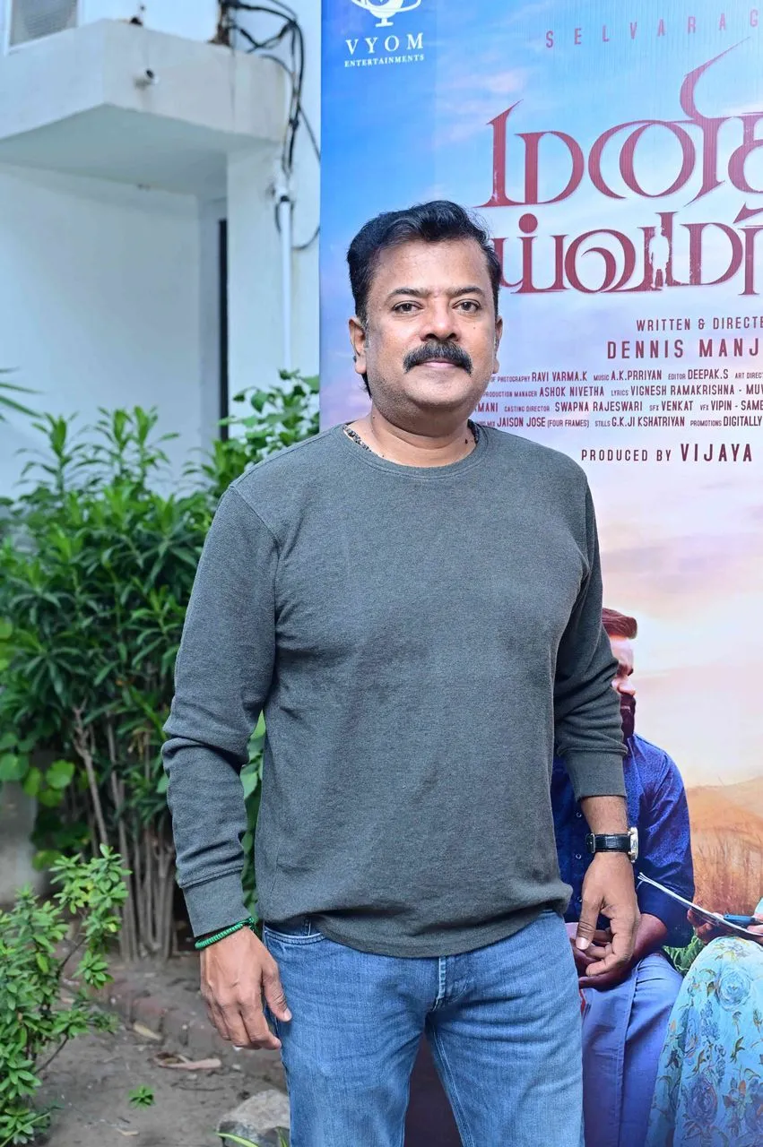 Selvaraghavan standing next to the Manithan Deivamagalam movie poster
