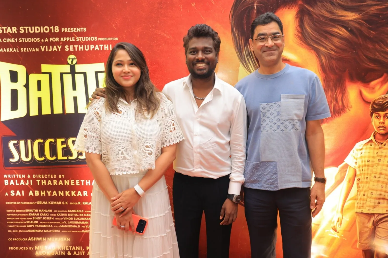 Three guests pose in front of the Baththa success meet backdrop